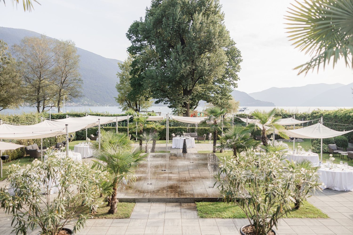 Elegant outdoor wedding venue setup with white shade sails and palm trees overlooking a mountain lake landscape.