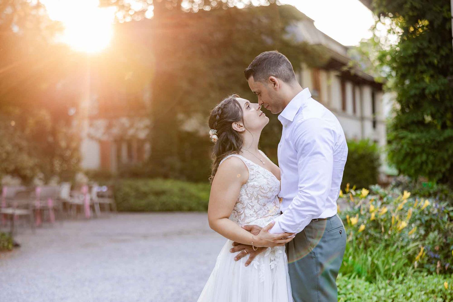 Bride and groom share a romantic moment at golden hour outside an elegant venue surrounded by lush gardens.