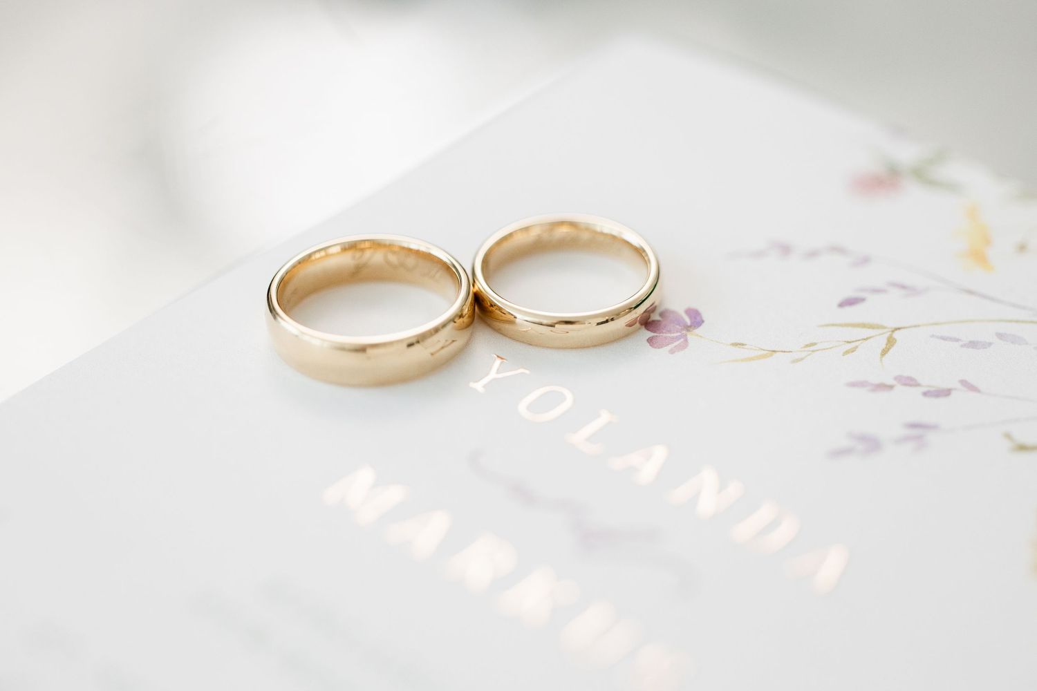 Two elegant gold wedding rings displayed on a soft white surface with delicate details in the background.