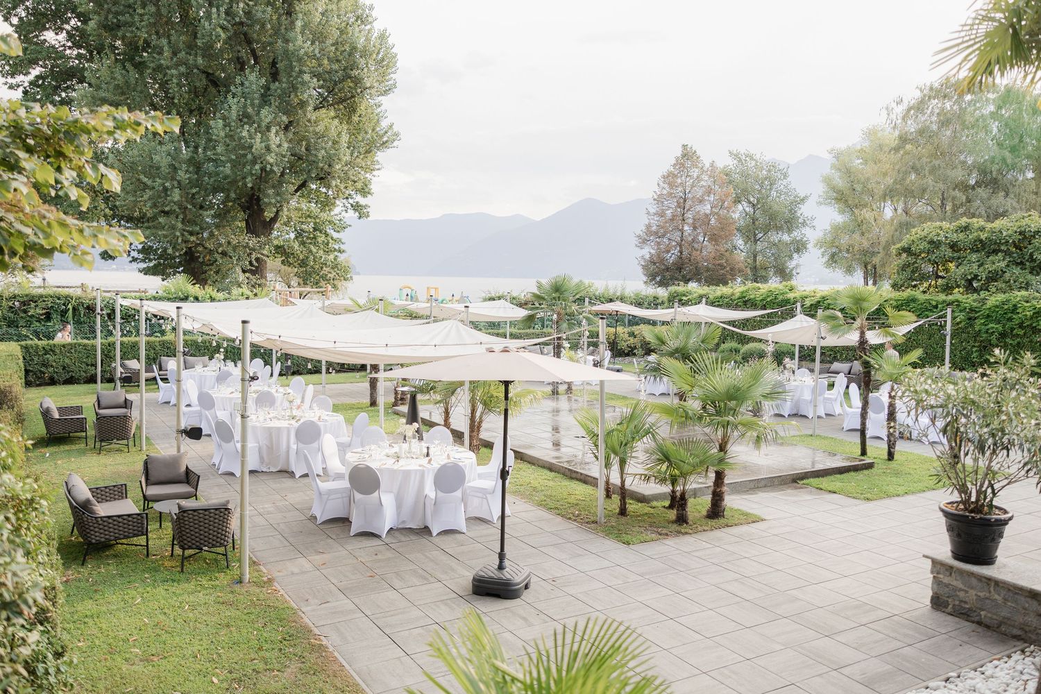 Elegant outdoor wedding venue setup with white covered tables overlooking a scenic waterfront view on a clear day.