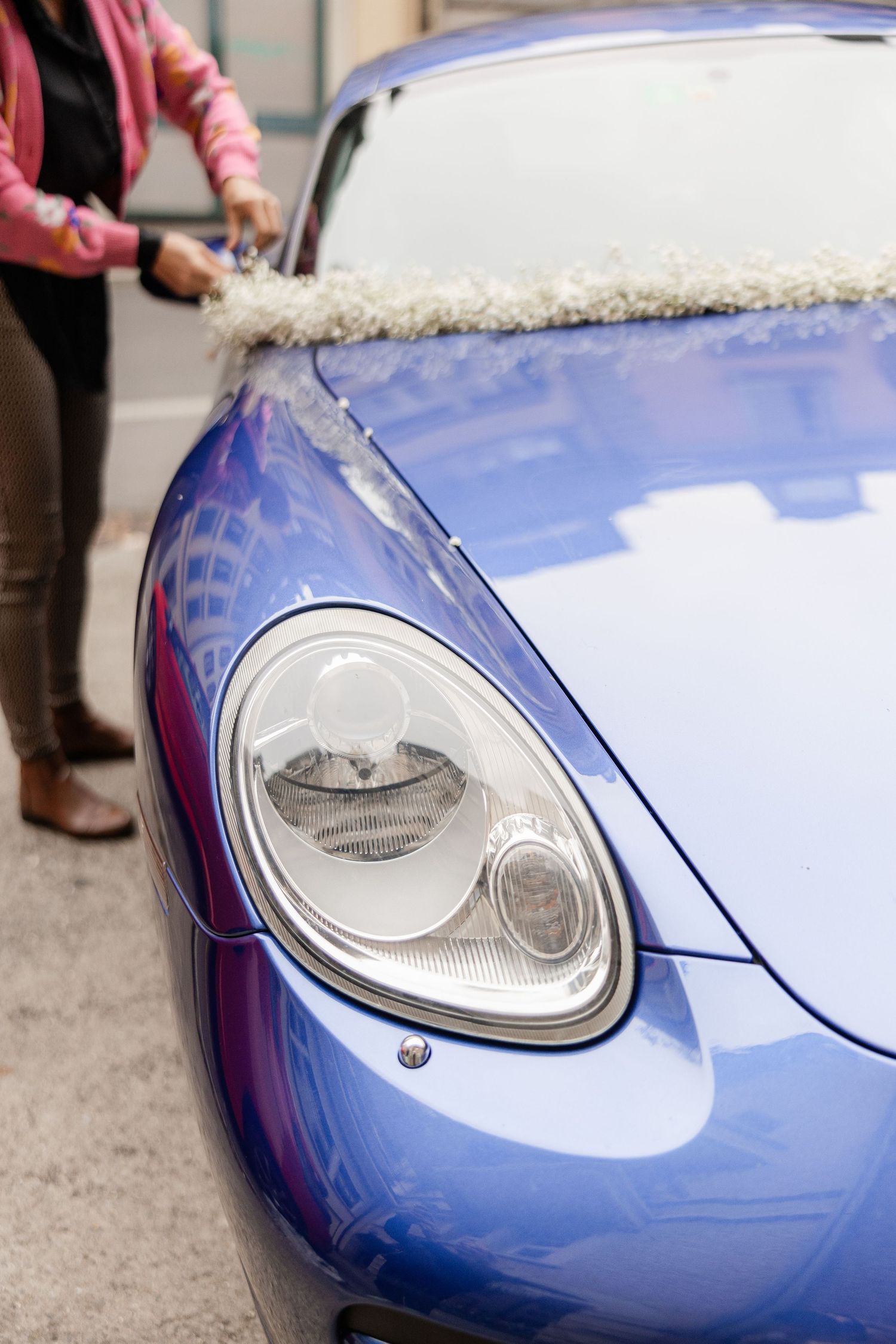 Someone washing the headlight and hood of a blue Porsche sports car with a cleaning cloth.
