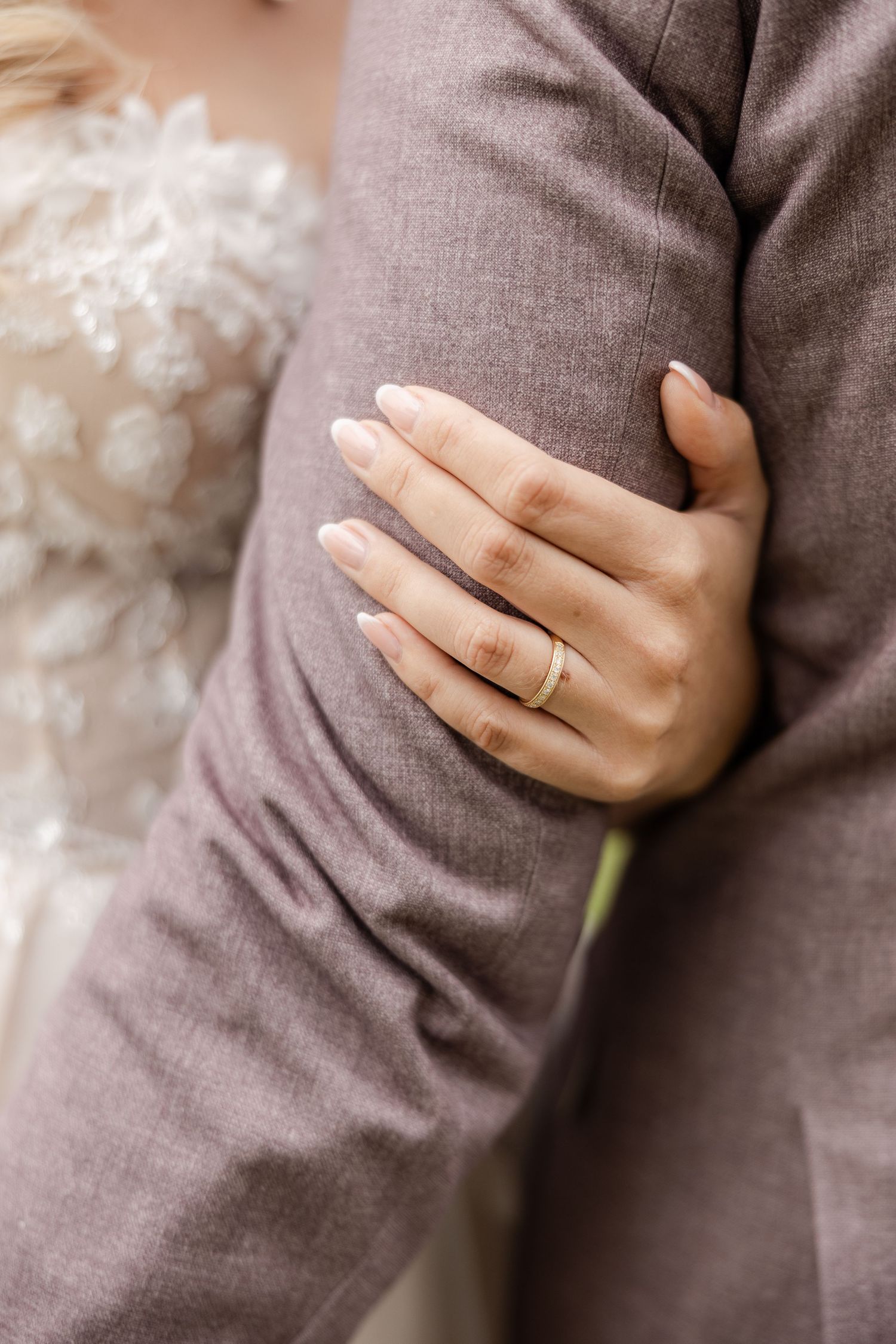 Close up view of hands wearing a simple gold wedding band against a soft gray fabric background.