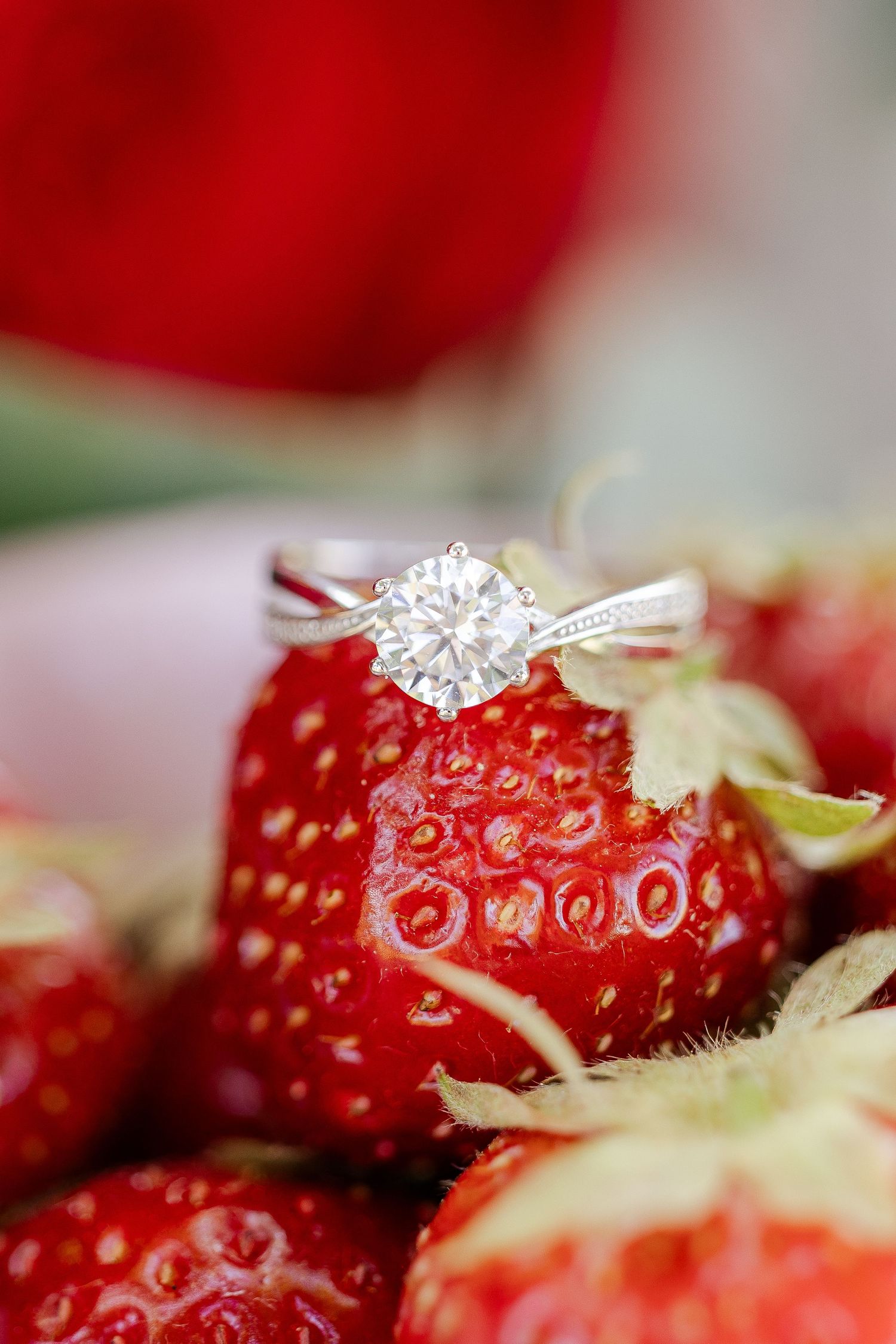 A sparkling diamond engagement ring elegantly placed on top of a fresh red strawberry in macro photography.