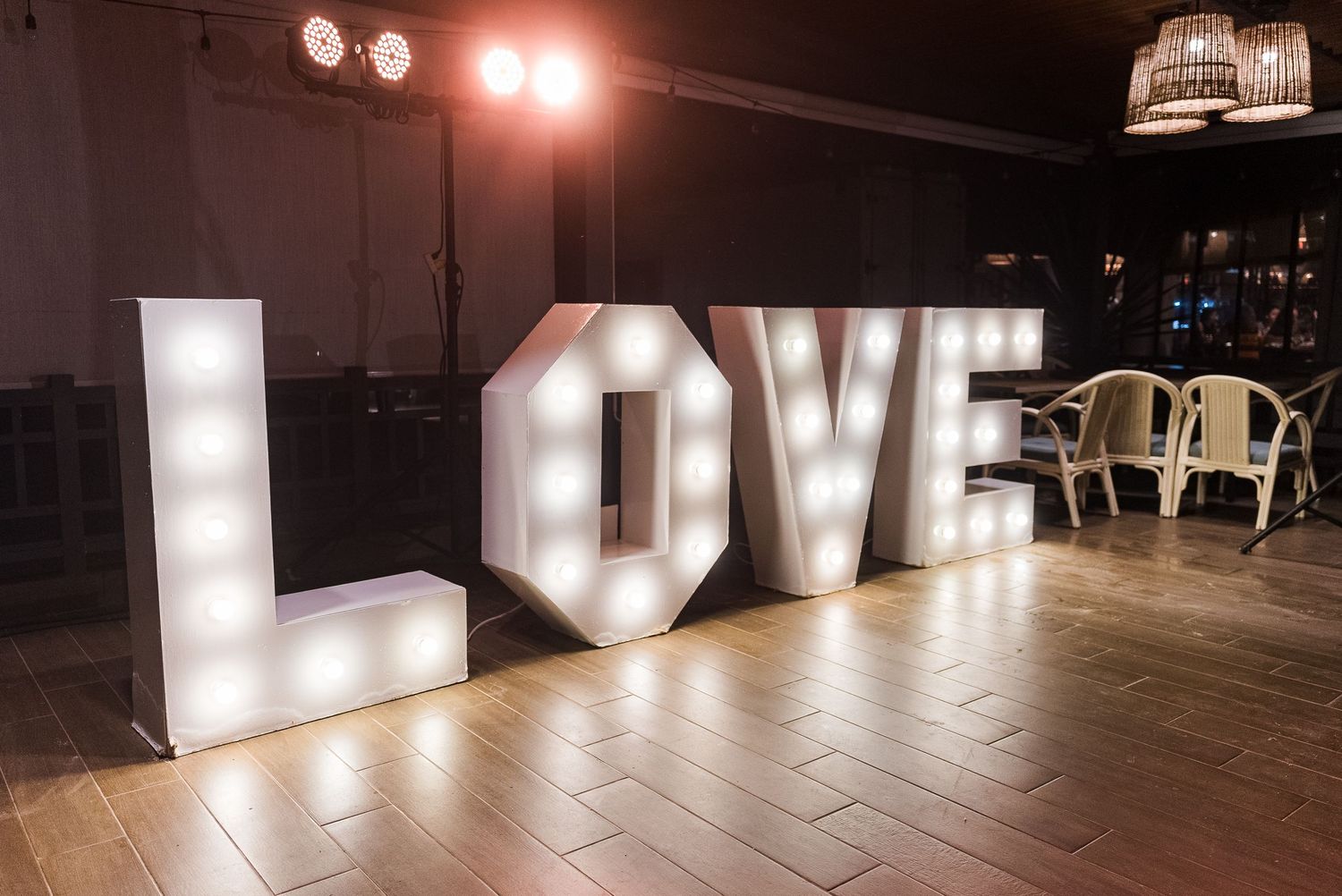 Large illuminated marquee LOVE letters with light bulbs displayed on a wooden dance floor at a wedding reception.