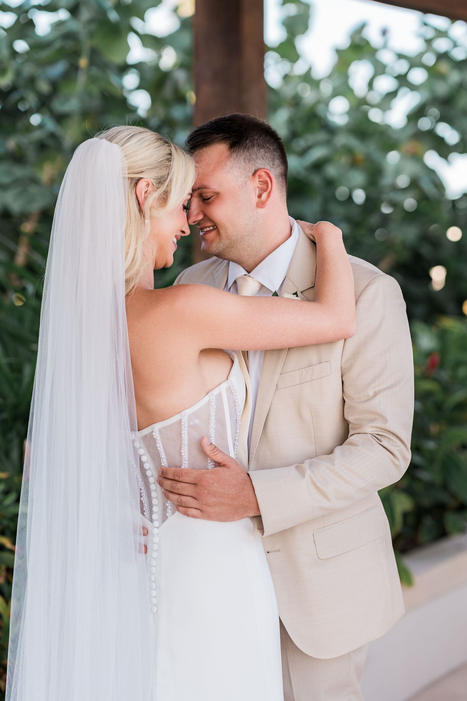 Bride and groom embrace tenderly during romantic first look at tropical garden wedding venue.
