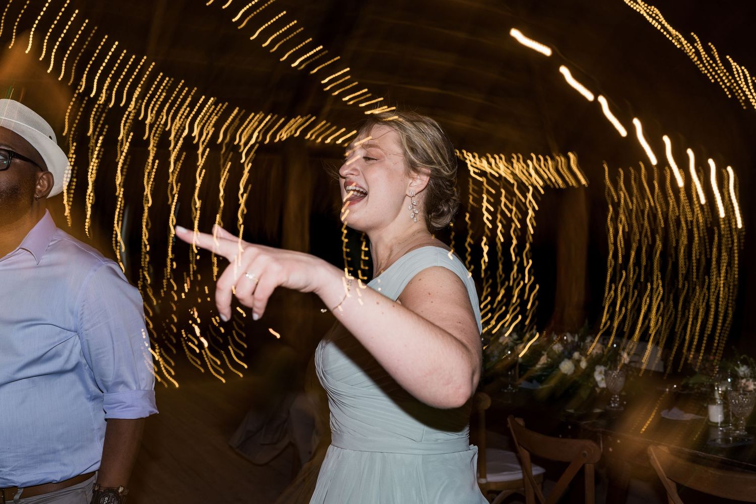 Bridesmaid in mint dress laughs and points during energetic wedding reception dance party.