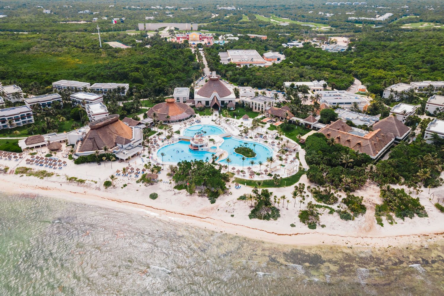 Aerial view of a luxurious beachfront resort with a large pool, chapel, and lush tropical surroundings.