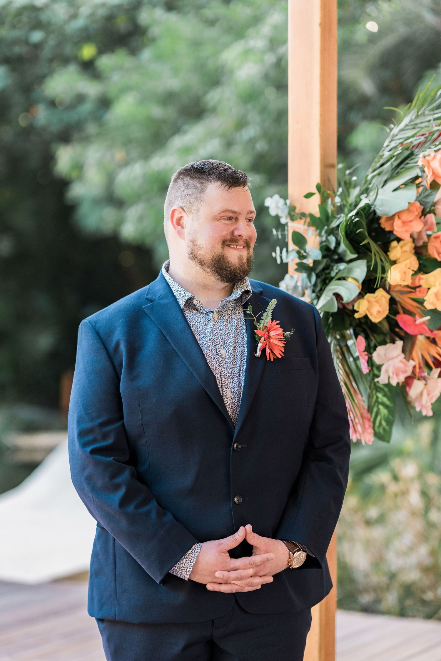 Secrets Akumal Wedding - Smiling groom in navy suit with coral boutonniere stands at outdoor wedding altar