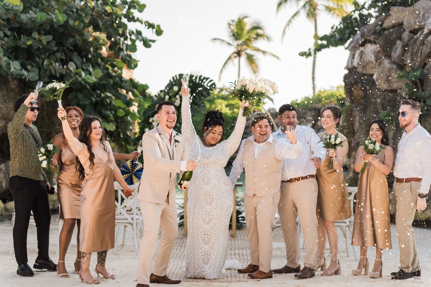 Xcaret Arte Wedding - Joyful wedding party celebrating on a tropical beach with palm trees, wearing neutral tones
