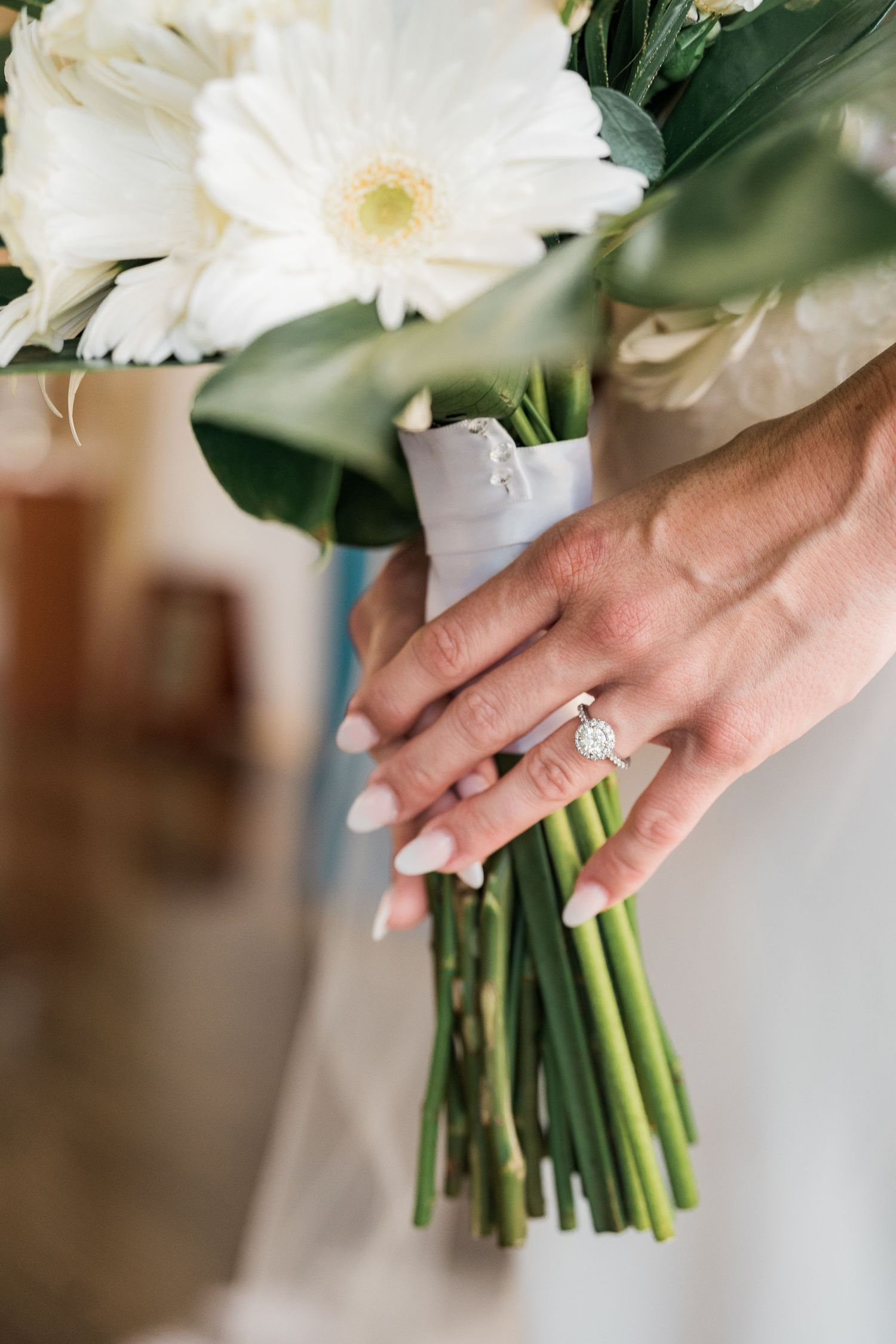 Bride holding white gerbera daisy bouquet with diamond engagement ring and white manicured nails.