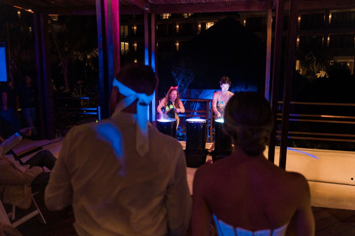 Couple watches performers on a glowing stage at an outdoor evening event with blue and purple lighting.