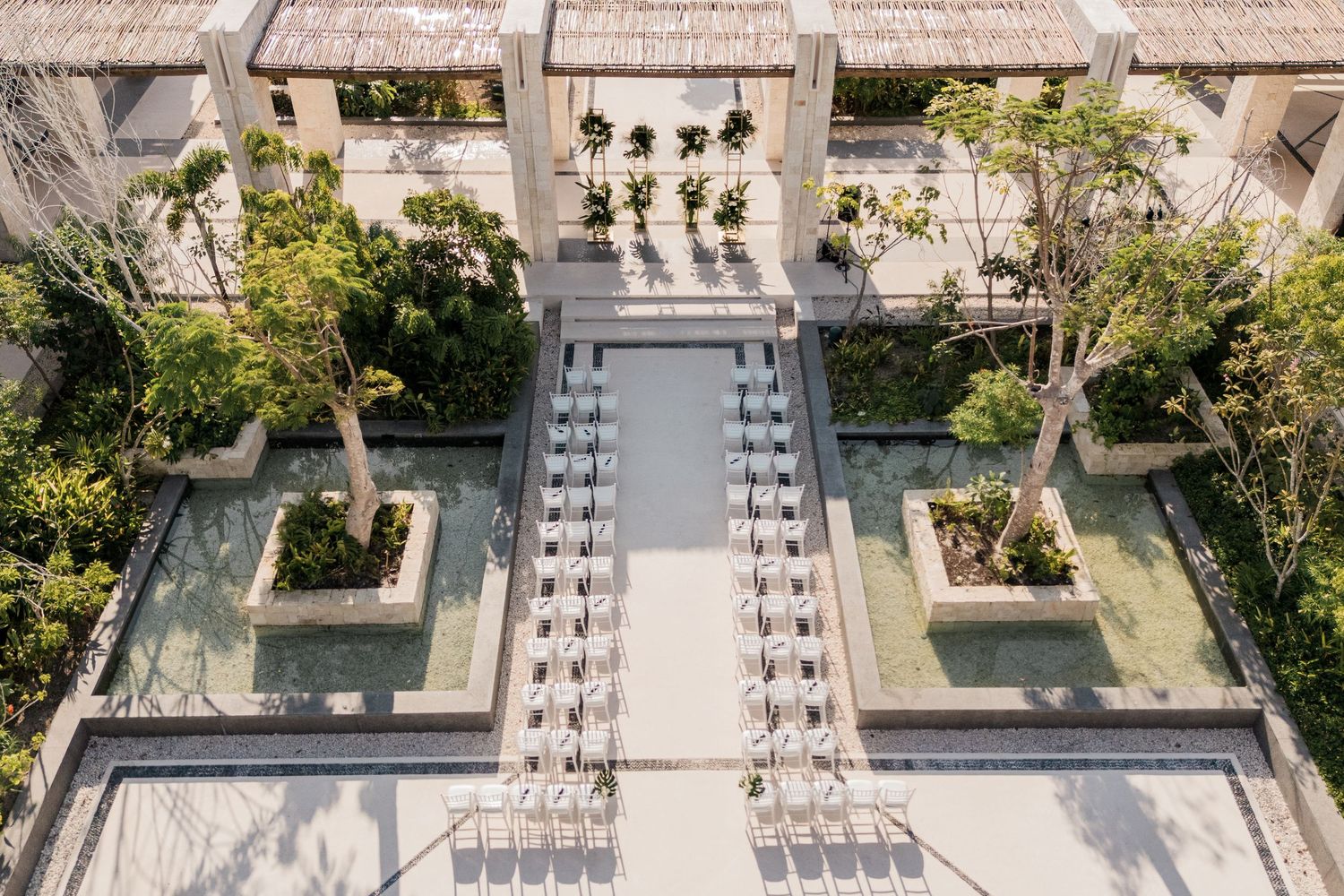 Aerial view of a luxury resort courtyard with symmetrical water features, lounge chairs, and lush tropical trees.