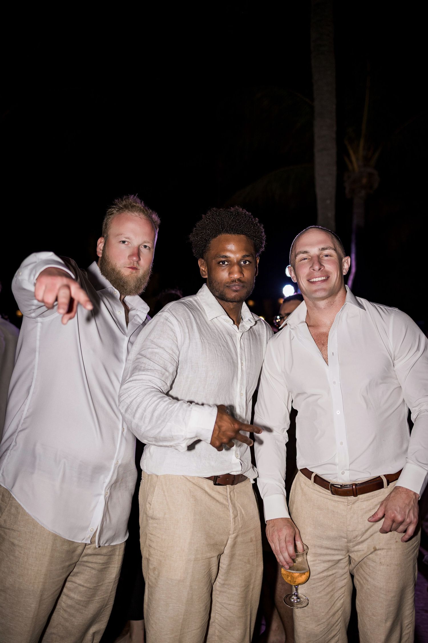 Three men in white shirts and khaki pants posing together at an outdoor nighttime event.
