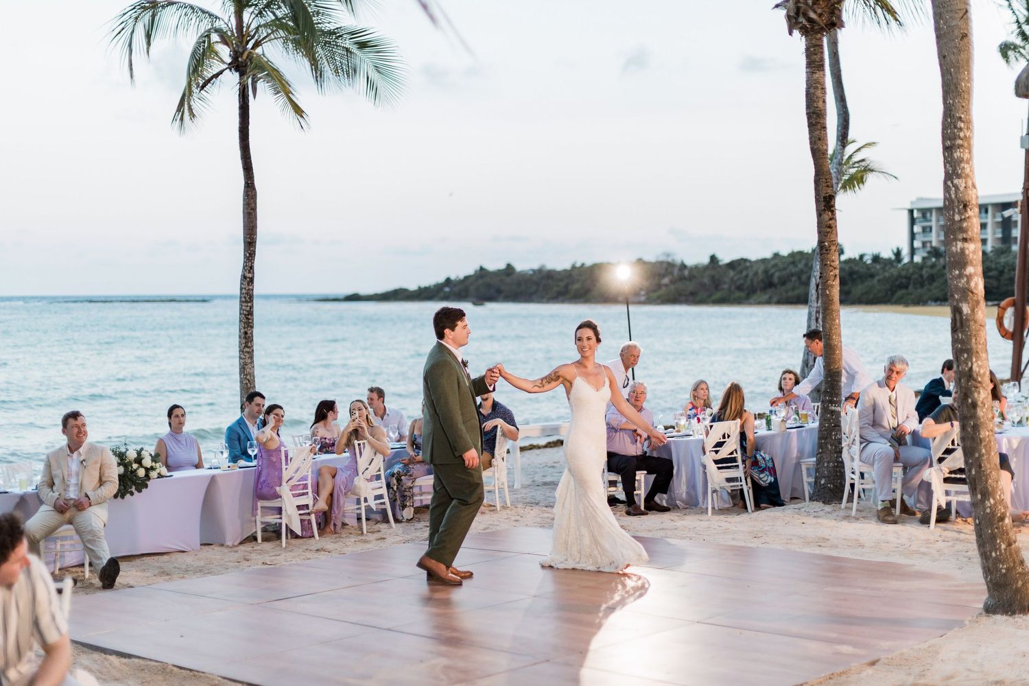 Bride and groom share first dance on beachfront dance floor at tropical outdoor wedding reception in Hawaii.