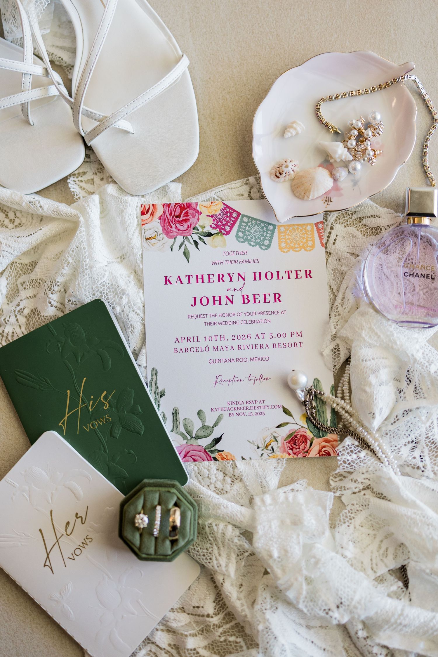 Wedding flat lay with floral invitation for Katheryn Holter and John Beer, vow books, rings, pearls, and Chanel perfume.