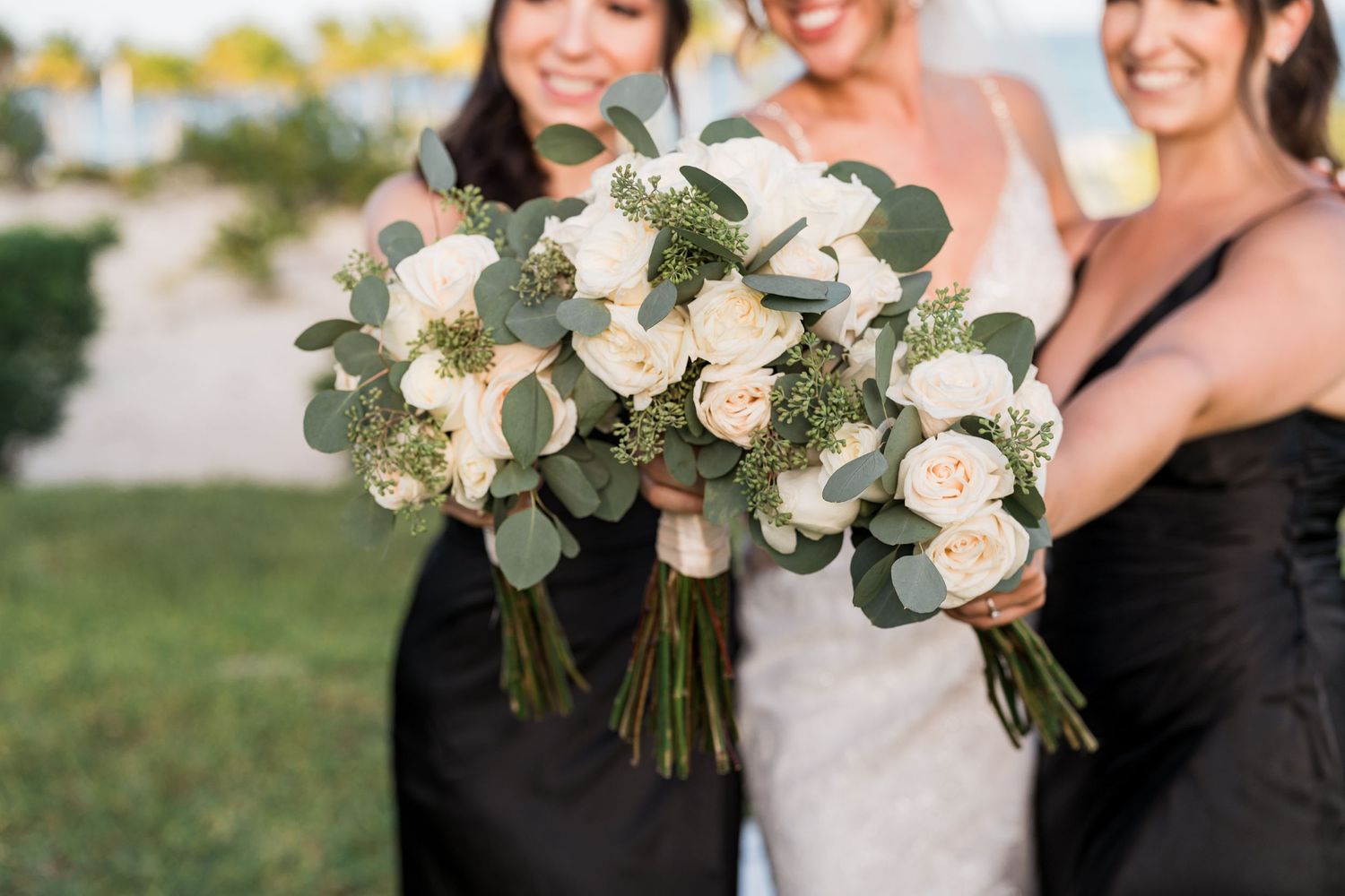 Close-up of elegant white rose and eucalyptus bridal bouquets held by bride and bridesmaids outdoors.