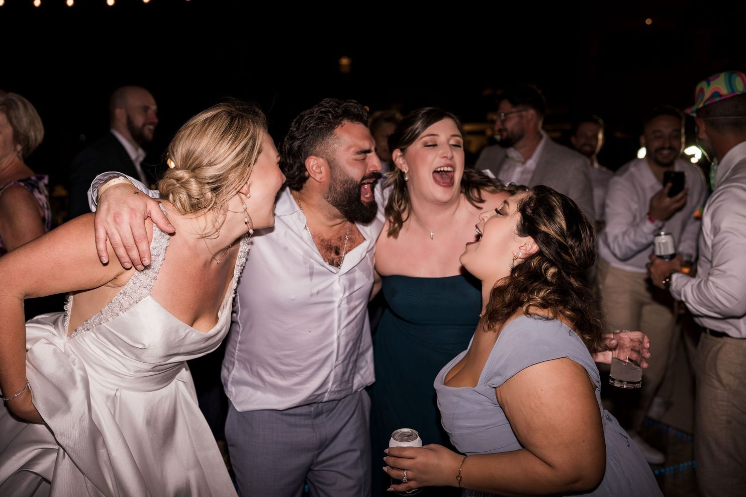 Wedding guests dancing and singing together joyfully at a lively outdoor wedding reception celebration.