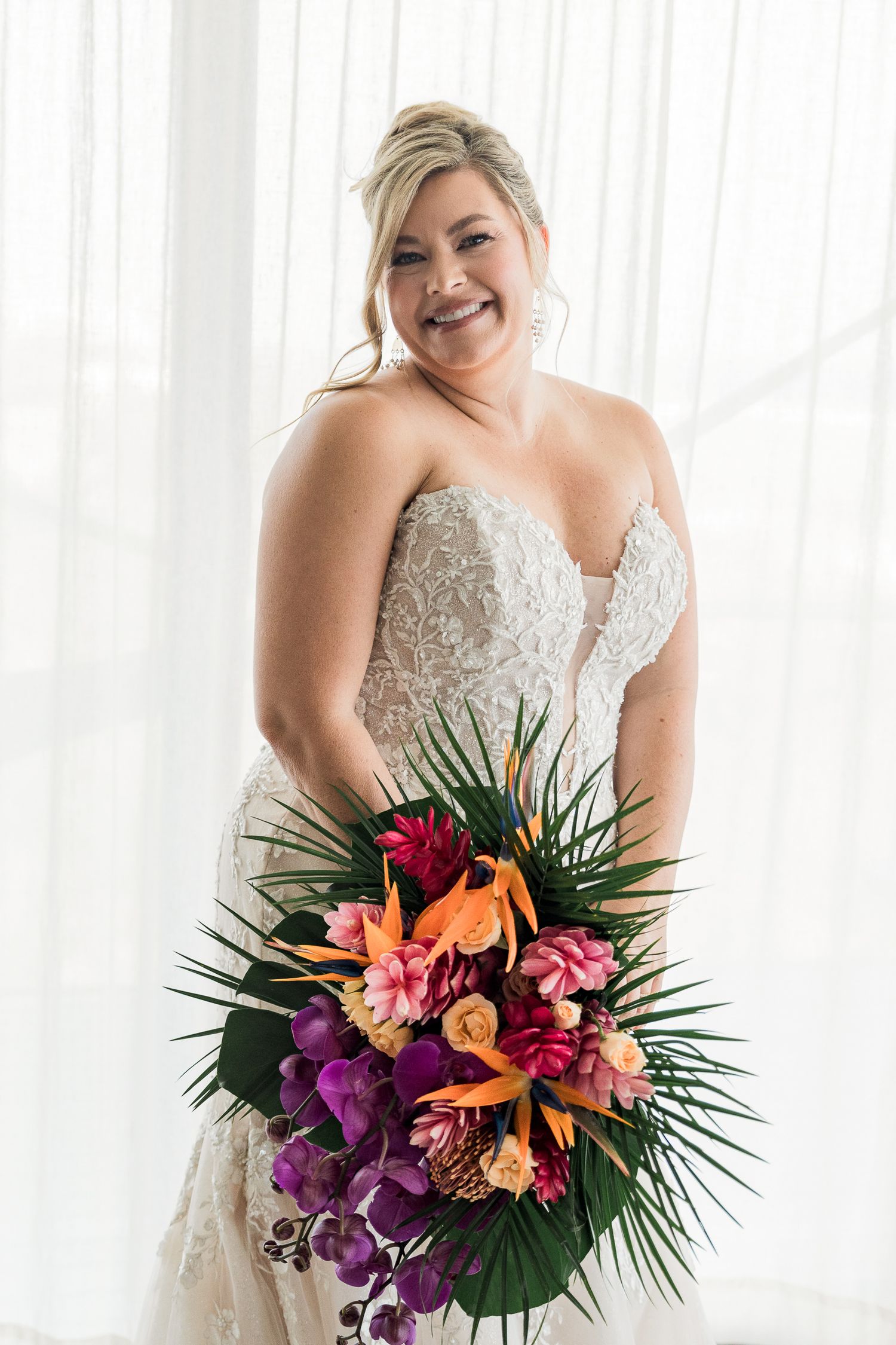 Hotel Xcaret México Wwedding - Smiling bride in strapless lace gown holding vibrant tropical bouquet with orchids