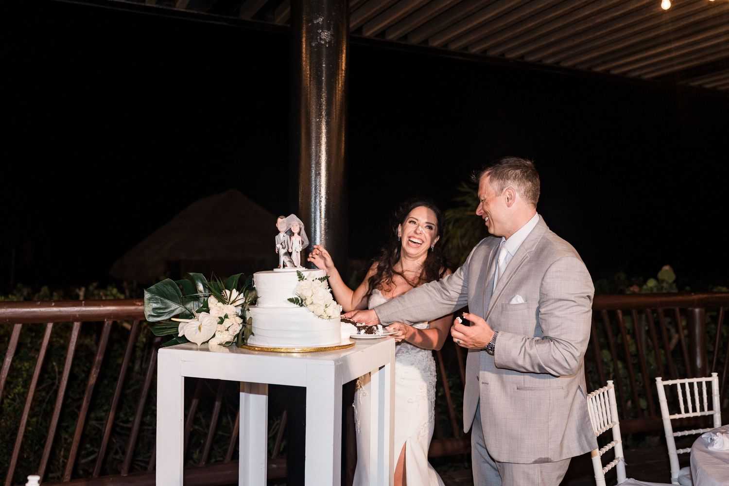 Bride and groom cutting their white wedding cake together at an outdoor evening reception.