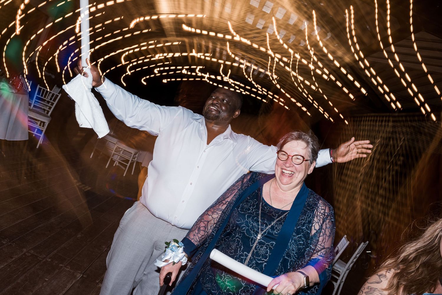 Joyful wedding reception guests dancing under twinkling fairy lights tunnel at night celebration.