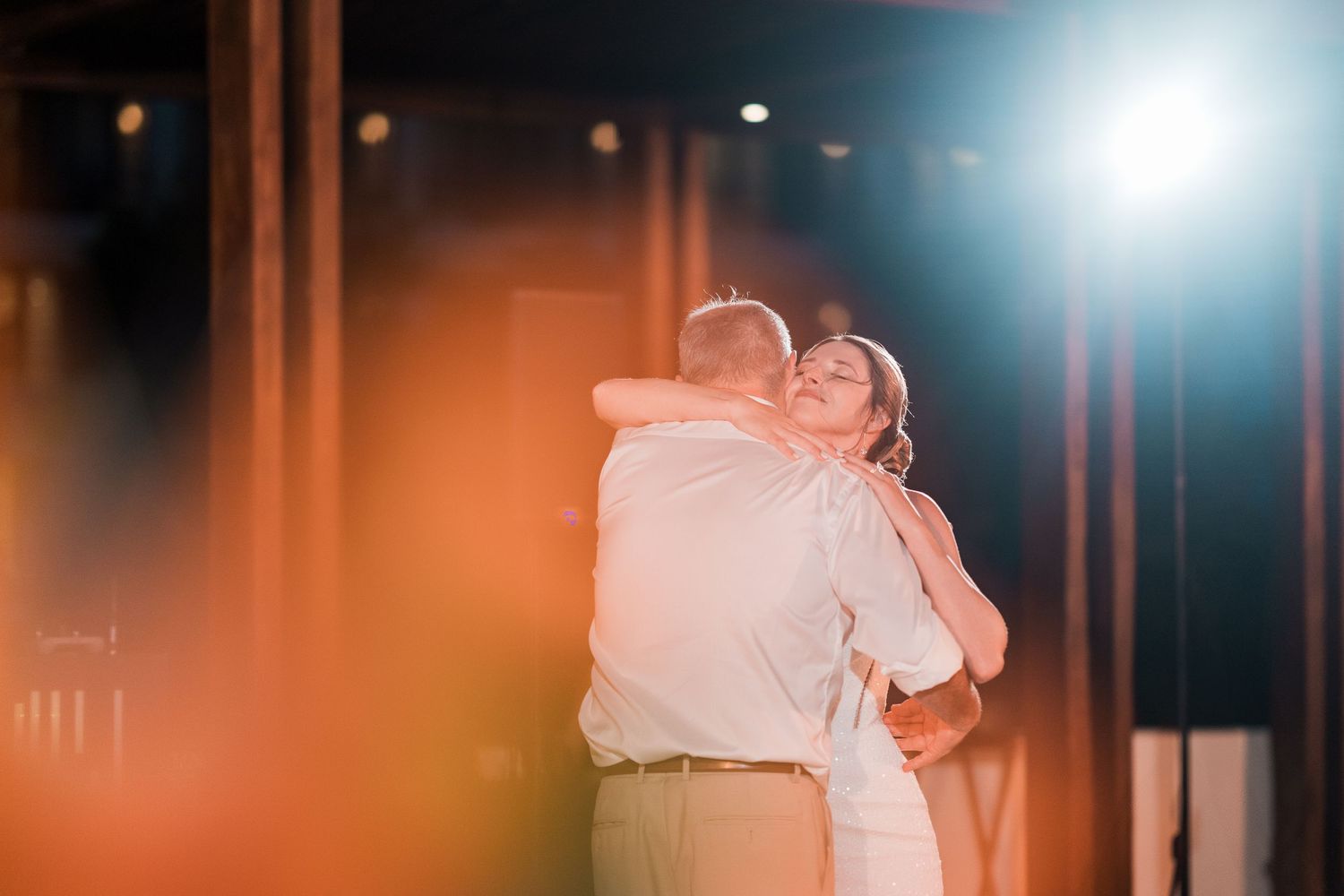 Bride and groom share an emotional first dance embrace, bathed in warm golden light at their wedding reception.