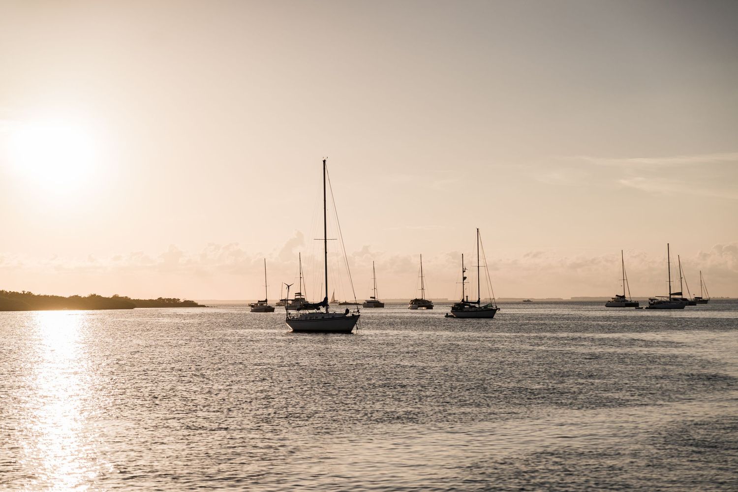 Sailboats anchored in calm waters at golden sunset, with soft glowing light reflecting on the sea.