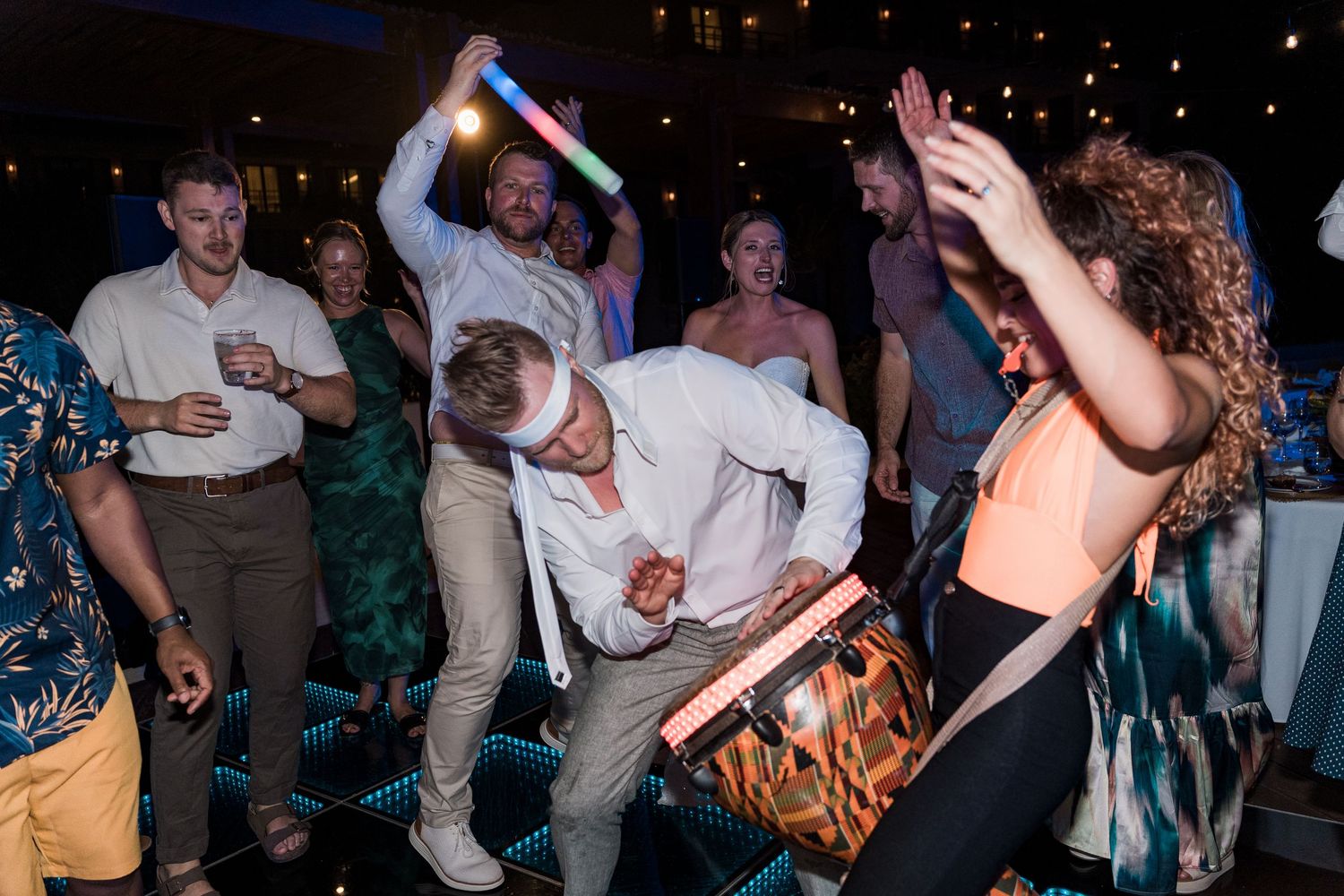 Guests dancing energetically at a lively wedding reception party with colorful lights and glow sticks.