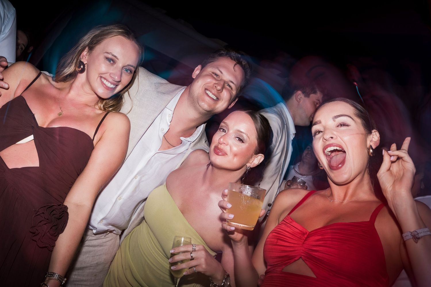 Group of friends smiling and posing together at a lively party, holding drinks and enjoying the festive atmosphere.