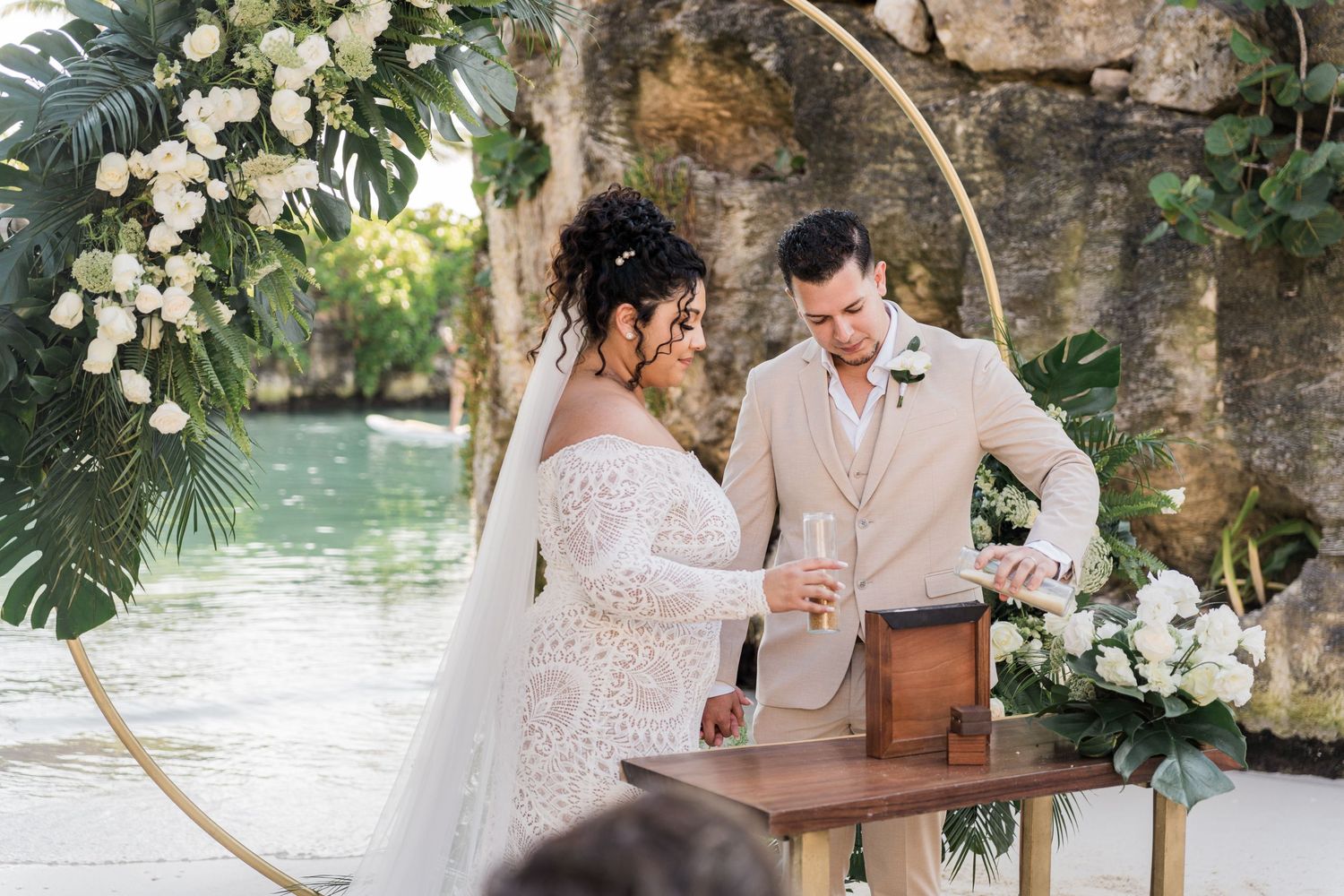 Xcaret Arte Wedding - Bride and groom perform a sand ceremony at an outdoor beach wedding with a floral hoop arch backdrop.