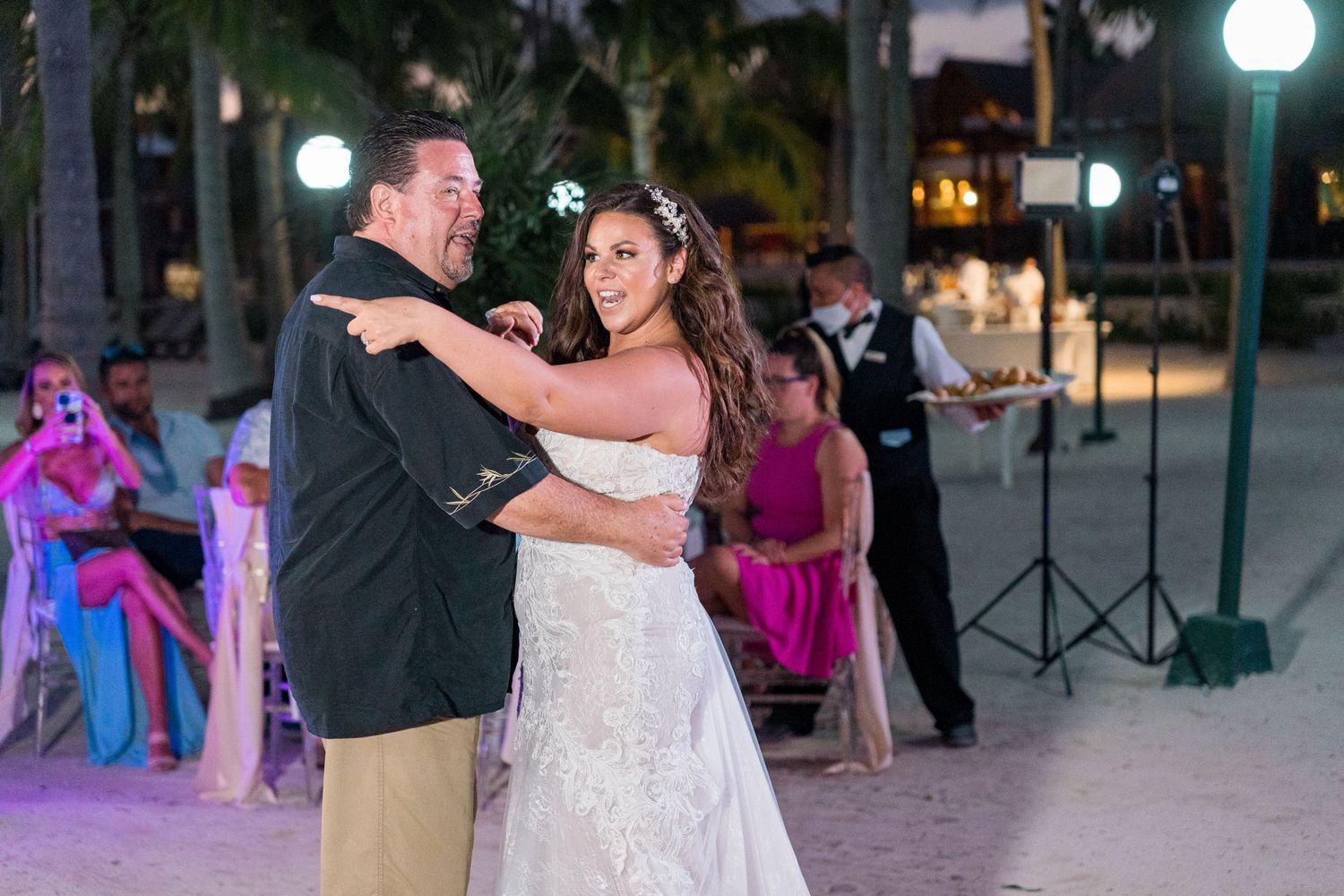 Bride and father share emotional first dance on tropical beach wedding reception at night.