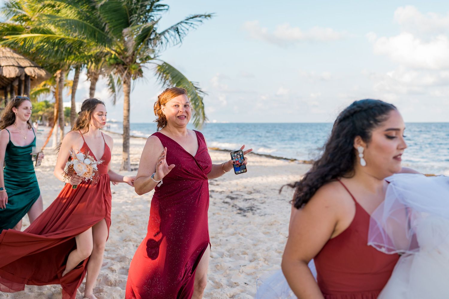 Bridesmaids in red dresses running and laughing on a tropical beach wedding celebration.