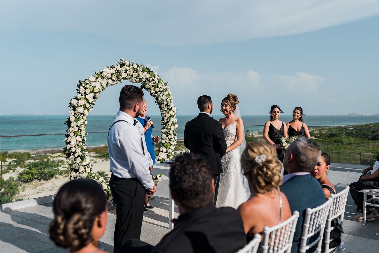 Bride and groom exchanging vows under a white floral arch at a stunning beachside wedding ceremony.