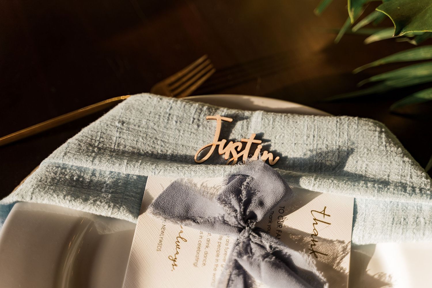 Elegant wedding place setting with laser-cut name tag reading Justin on folded linen napkin.
