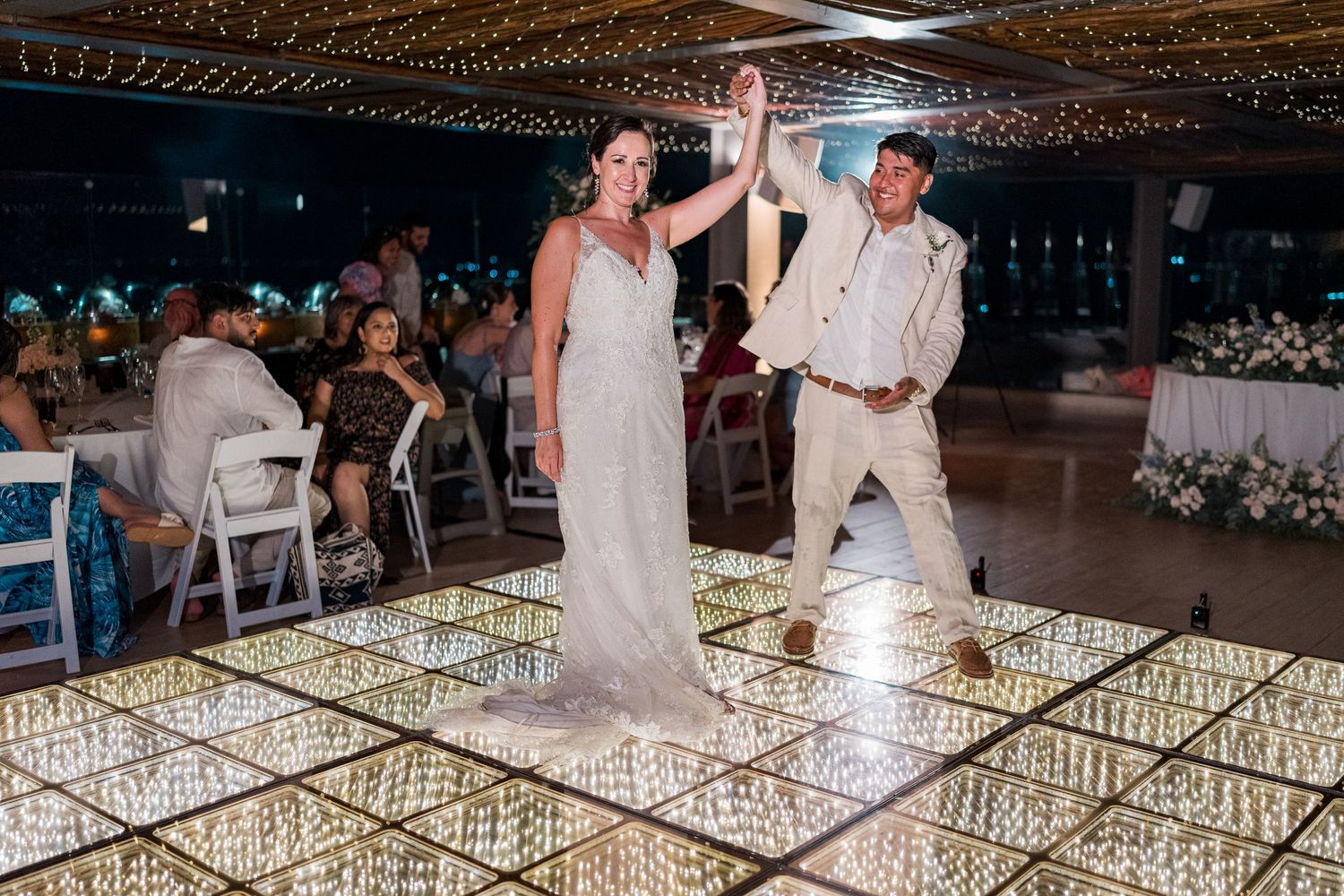 Bride and groom celebrate joyfully on a sparkling LED dance floor at their festive wedding reception.