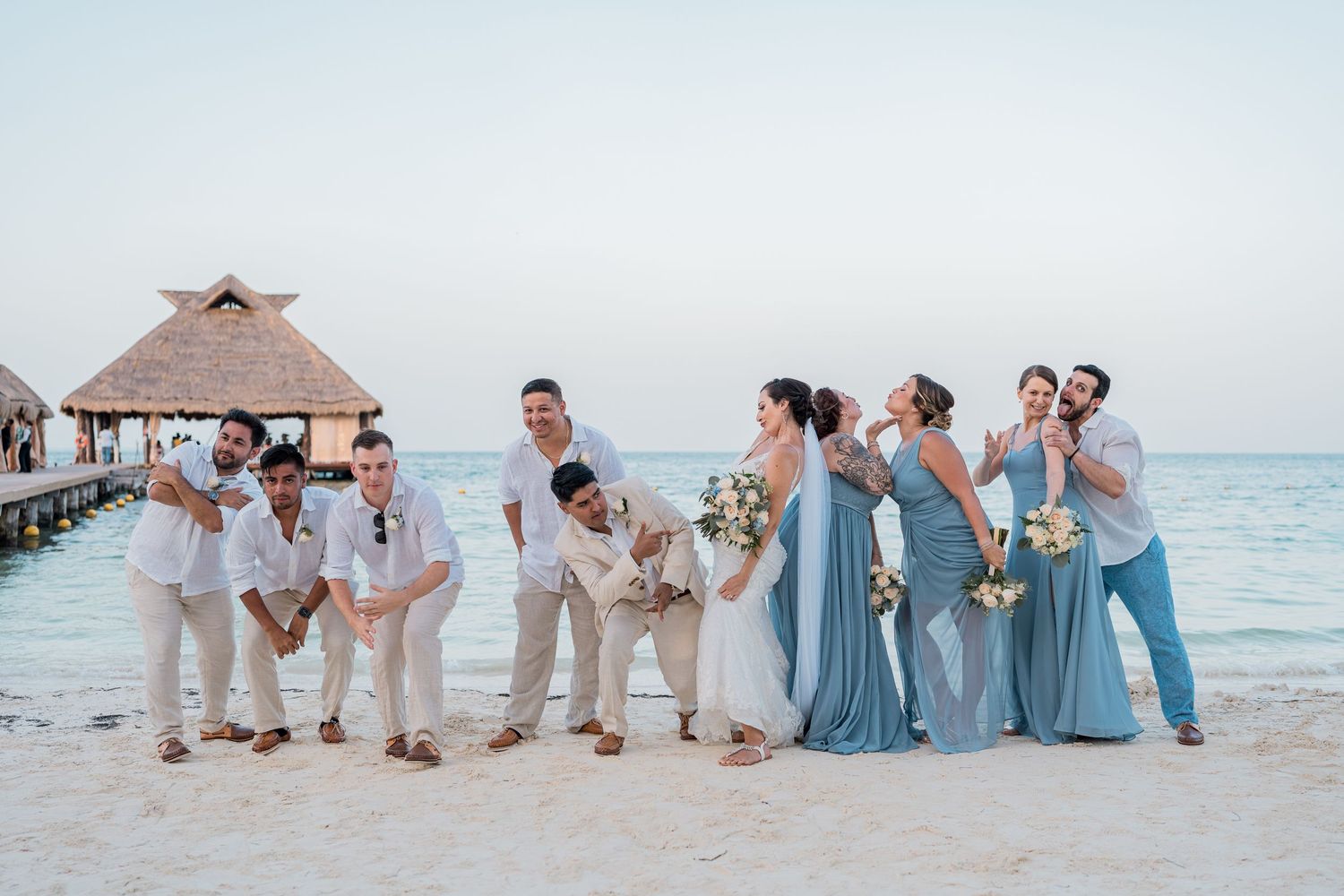 Bridal party laughs and poses candidly on sandy Caribbean beach during golden hour photos.
