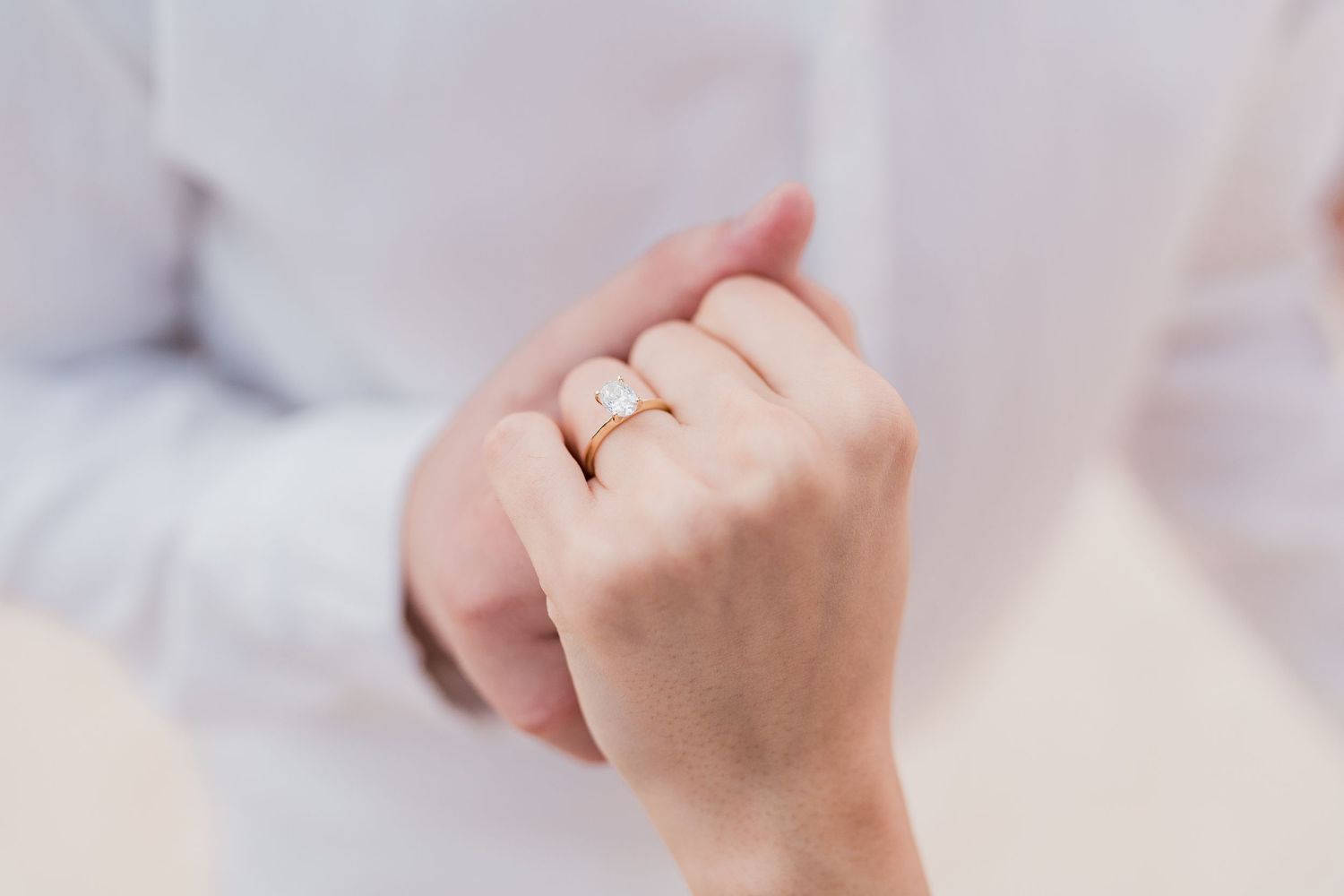 Close-up of a woman's hand wearing a gold engagement ring with a diamond solitaire, held by a man in a white shirt.