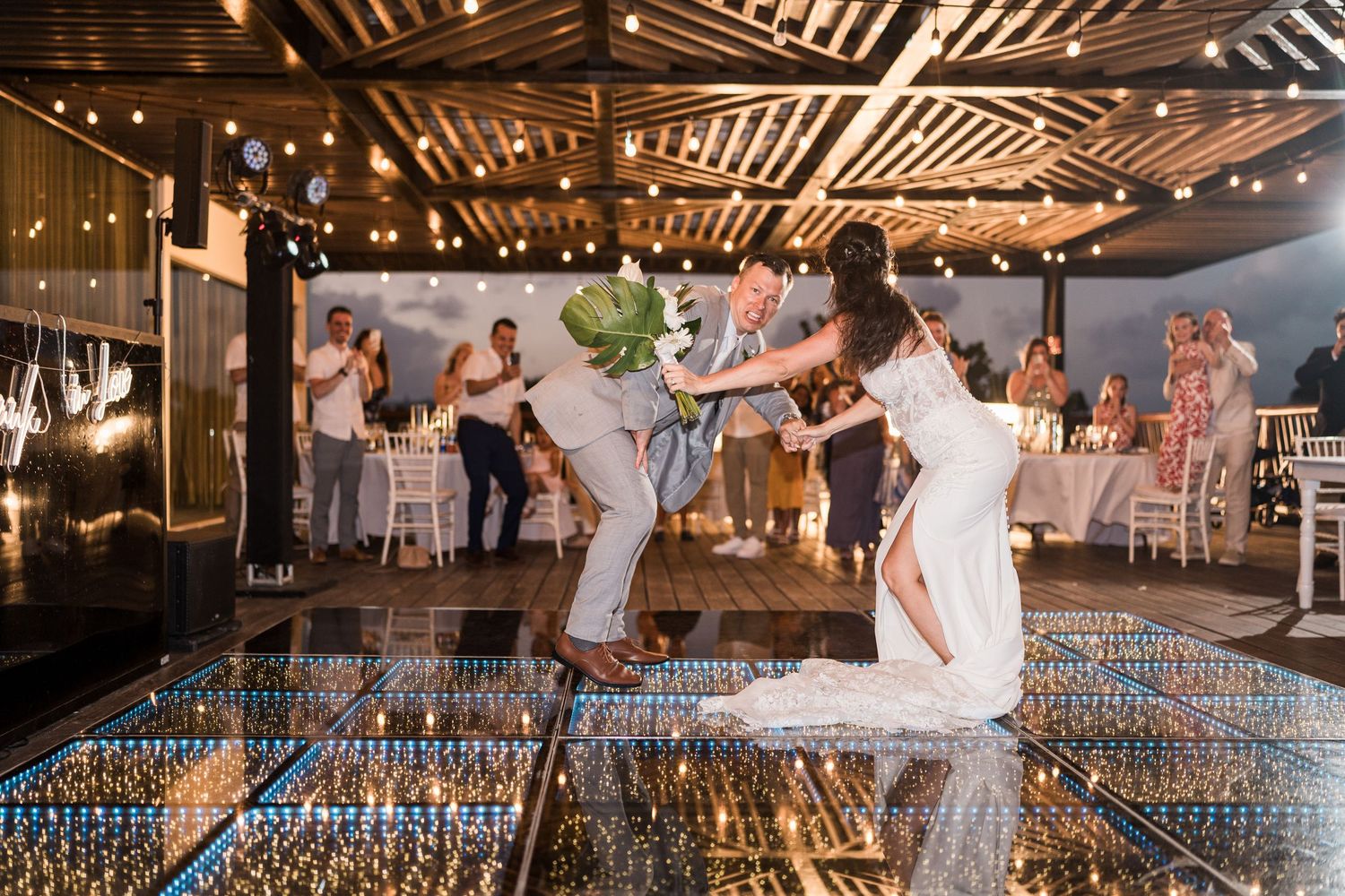 Bride and groom share a joyful first dance on a sparkling mirror floor at an elegant outdoor wedding reception.
