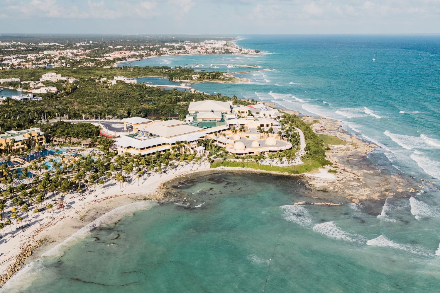 Aerial view of a tropical Caribbean coastline resort with turquoise waters, sandy beaches, and lush green palm trees.
