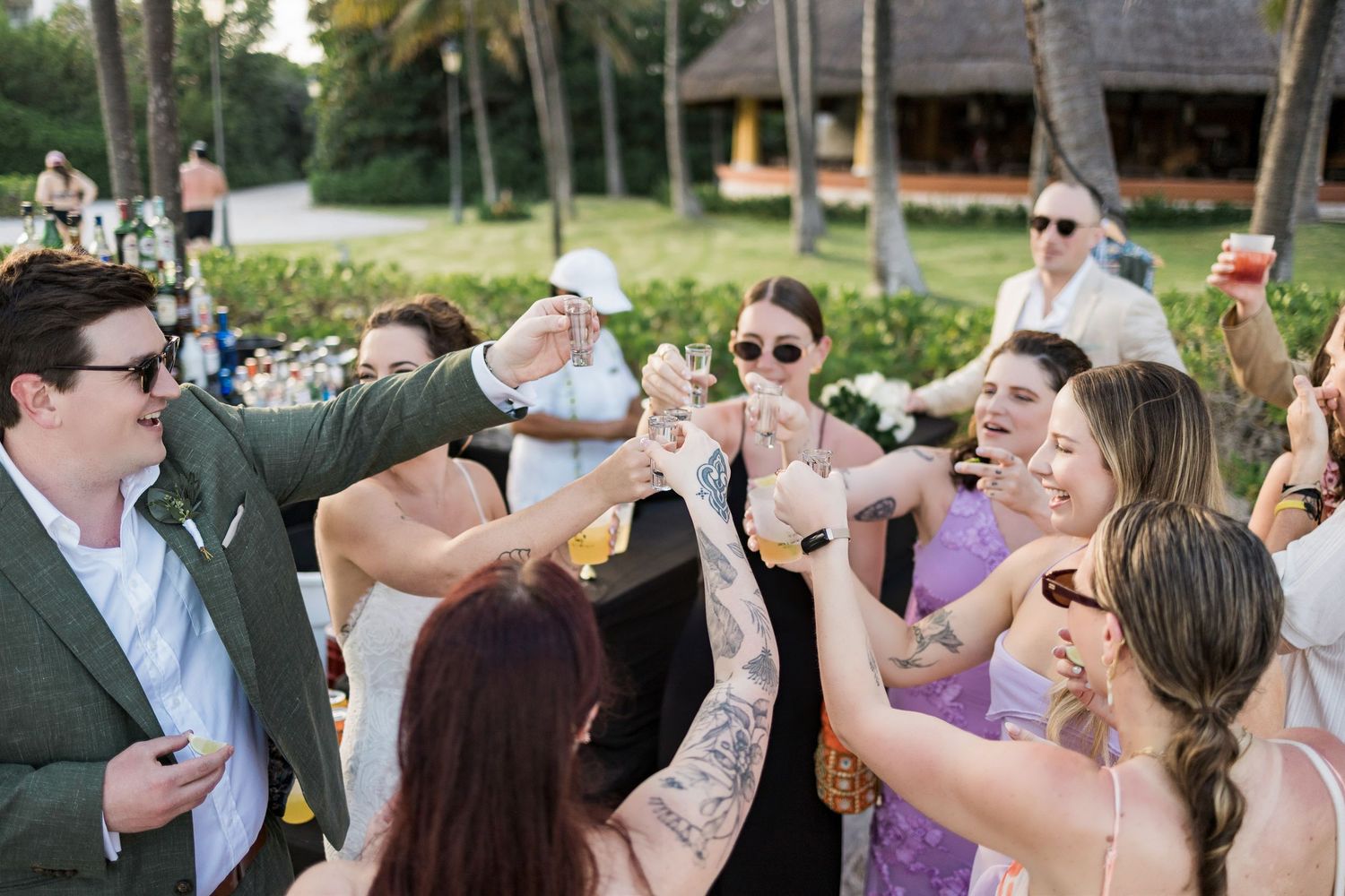 Guests raising glasses in a celebratory toast outdoors at a tropical wedding reception venue.