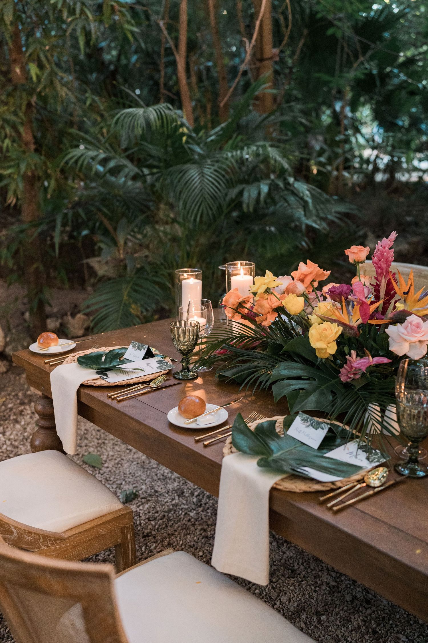 Secrets Akumal Wedding - Tropical outdoor wedding table with colorful floral centerpiece, candles, gold cutlery, and white runner