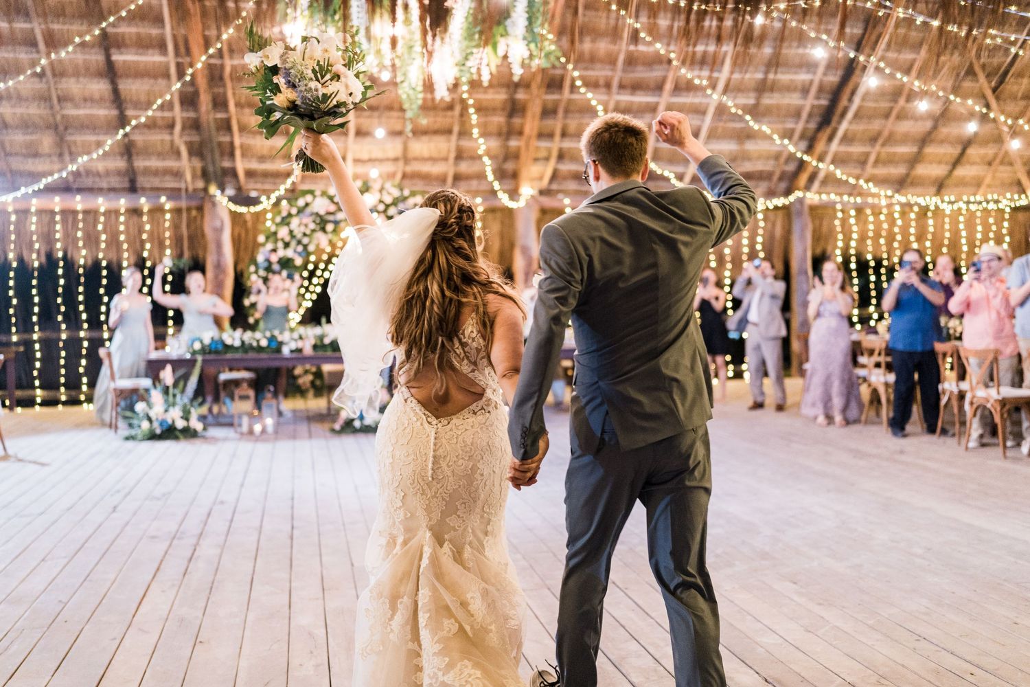 Bride and groom entering wedding reception under string lights in a rustic palapa venue.
