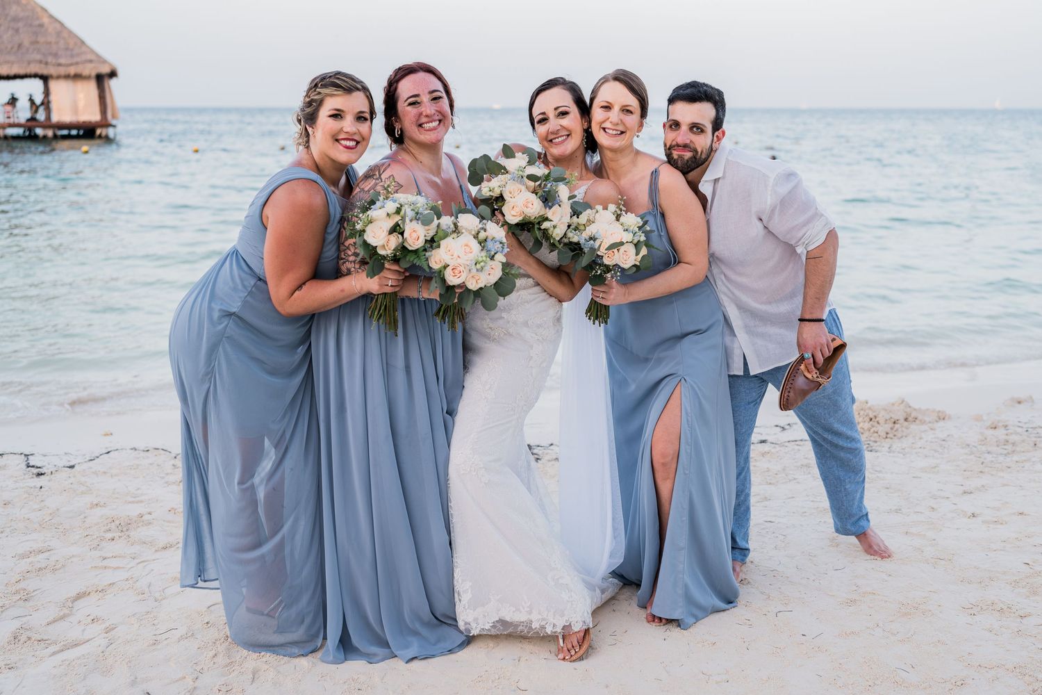 Wedding party laughing together on tropical beach at sunset.