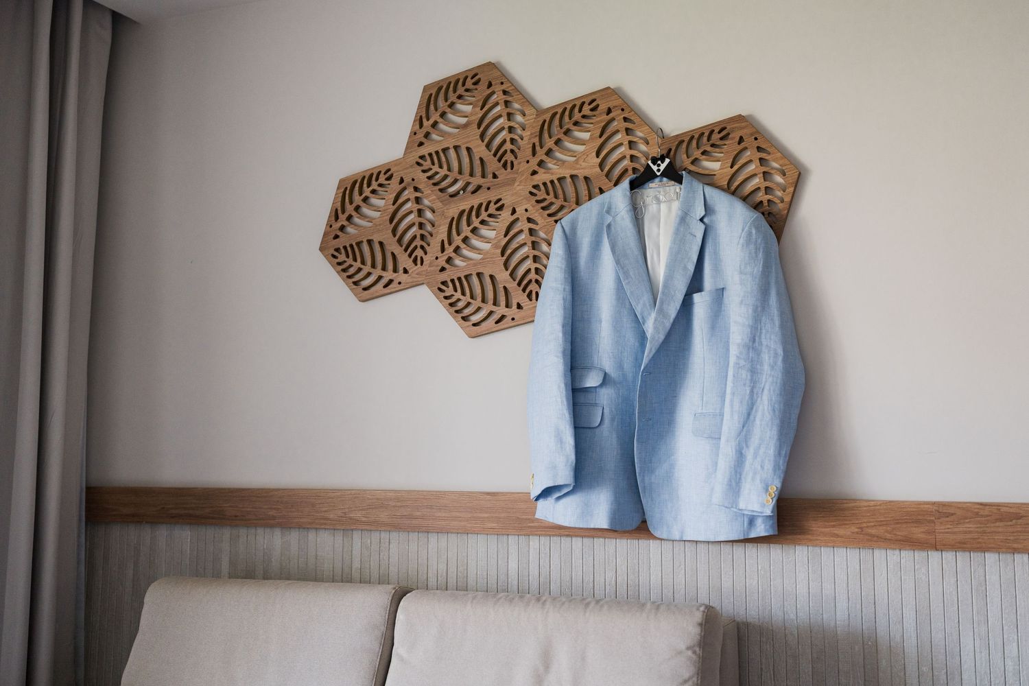 Light blue linen groom suit jacket hanging on decorative wooden wall shelf.