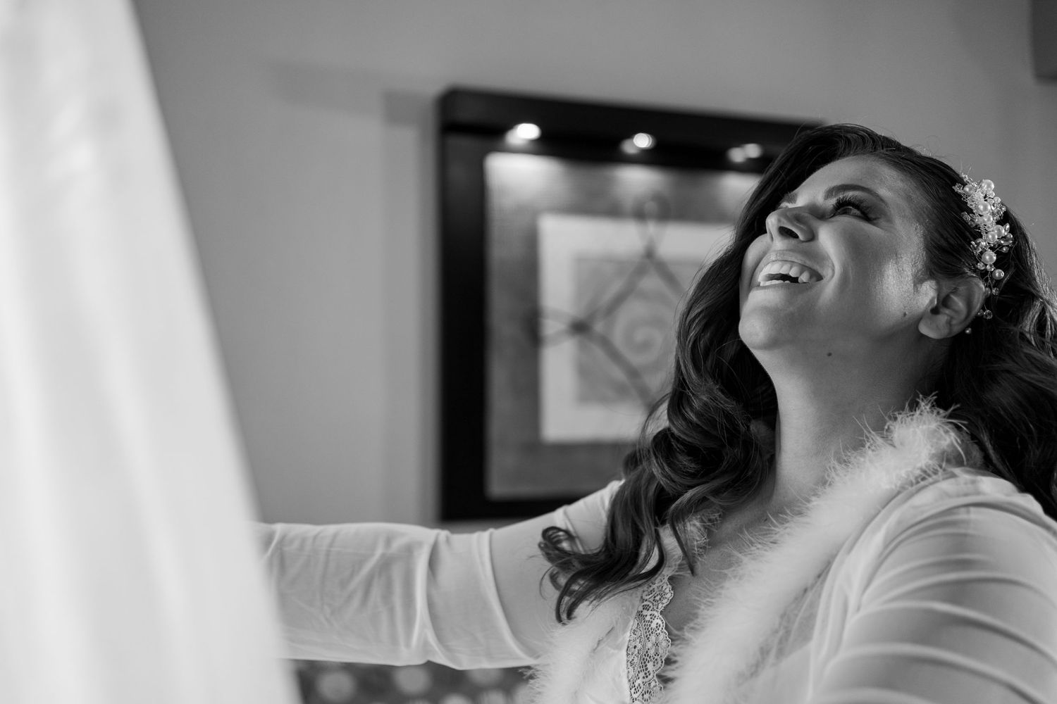 Black and white photo of a joyful bride laughing while getting ready on her wedding day.