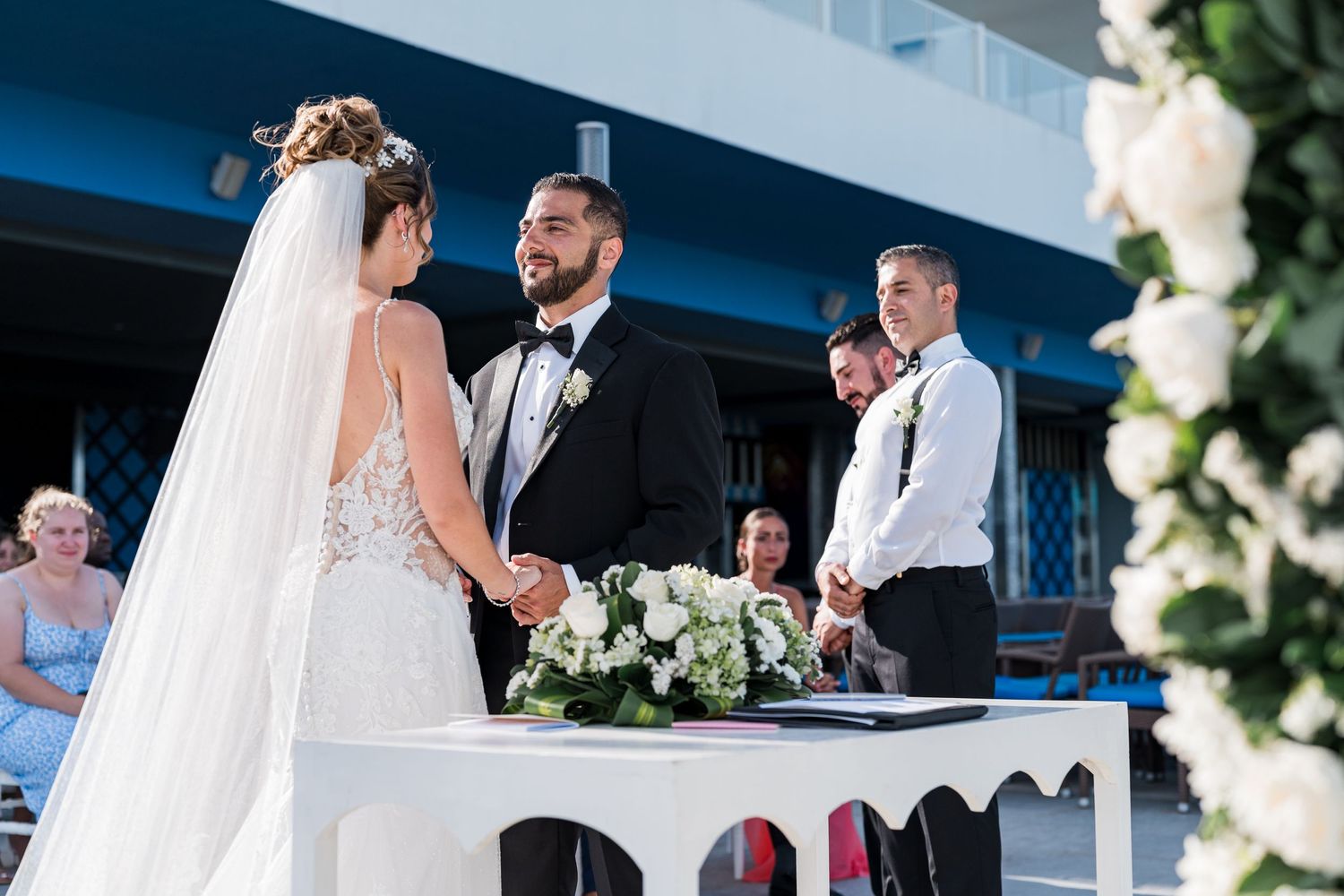 Bride and groom exchange vows at floral-decorated altar during outdoor wedding ceremony with smiling officiant.