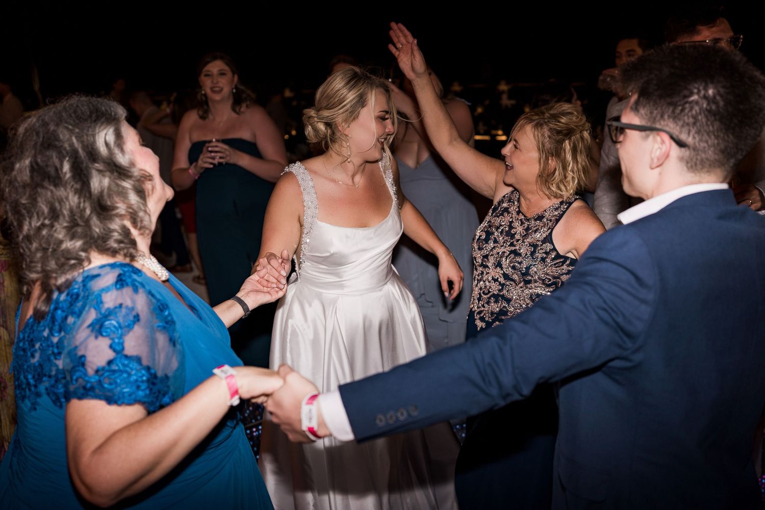 Bride in white gown dancing joyfully with wedding guests at a lively indoor reception celebration.