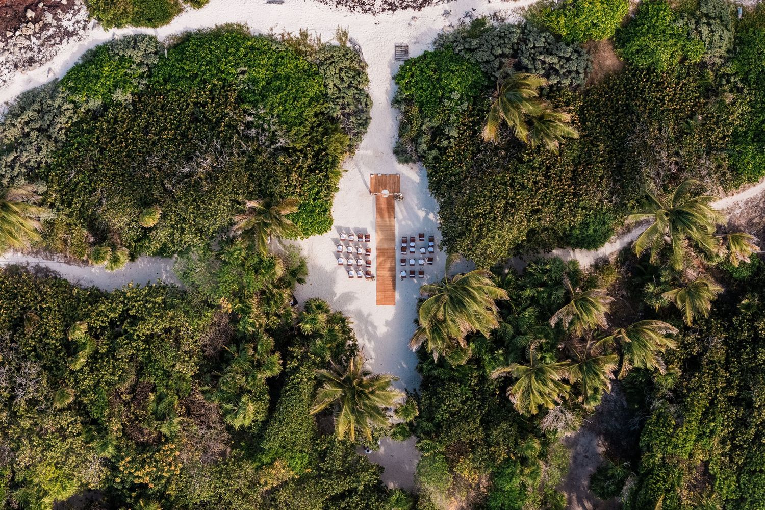Aerial view of a tropical beach resort nestled among lush palm trees and white sandy paths in a coastal setting at Akumal Bar Resort