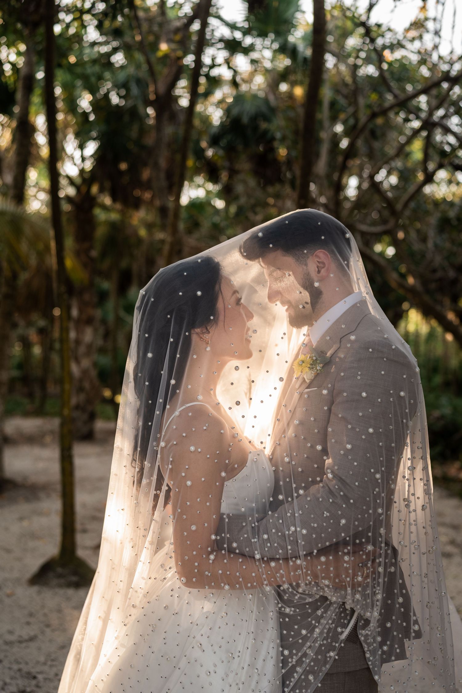 Bride and groom share romantic moment under polka dot veil surrounded by lush tropical trees at golden hour at Akumal Bay resort