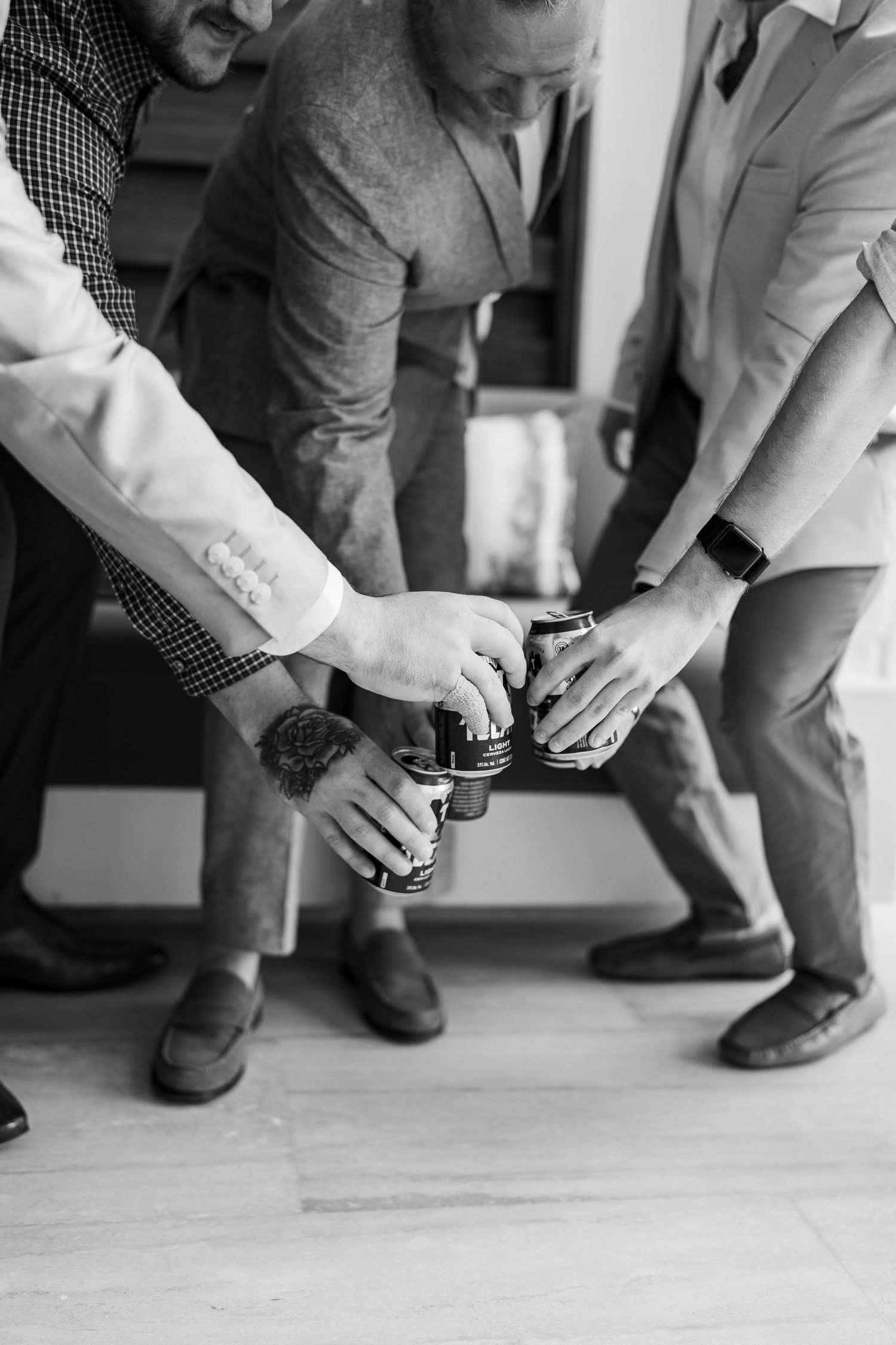 Black and white photo of men in suits clinking beer cans together in a celebratory toast.