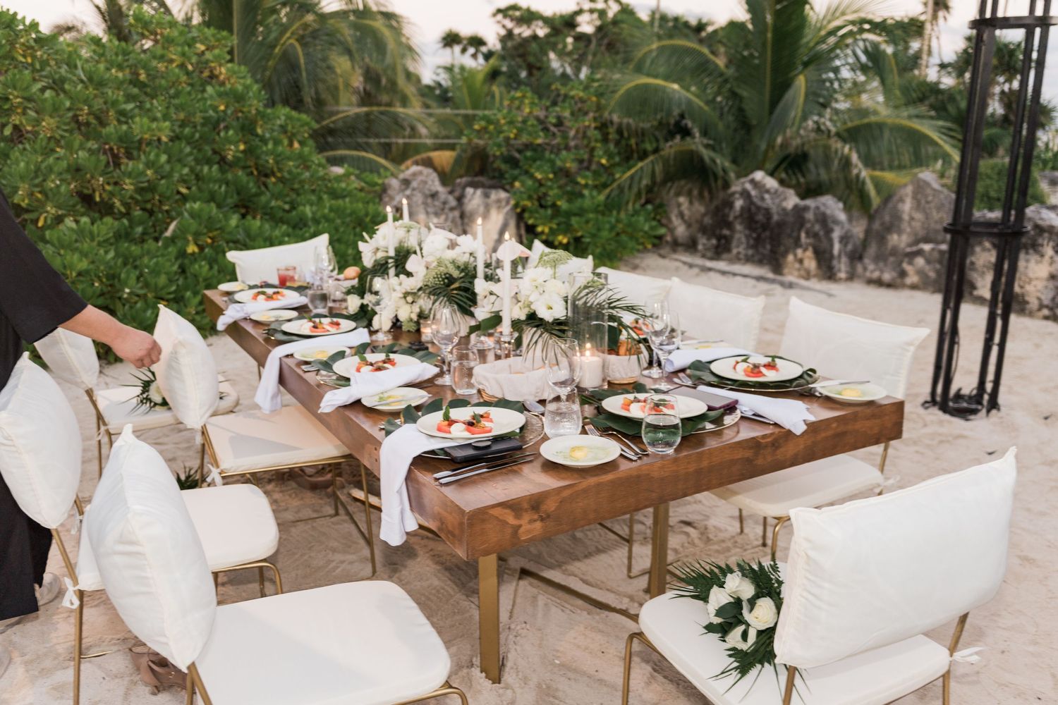 Xcaret Arte Wedding Elegant outdoor wedding reception table with white floral centerpieces, black plates, and gold chairs
